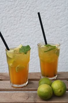 two glasses filled with lemonade and limes on top of a wooden table next to each other