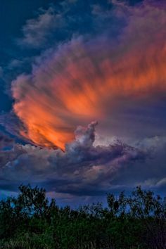 an orange and purple cloud is in the sky above some trees at sunset or dawn