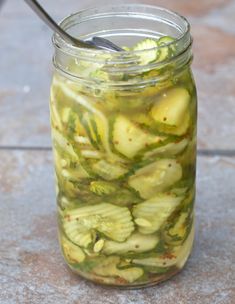 a jar filled with pickles sitting on top of a tile floor next to a spoon