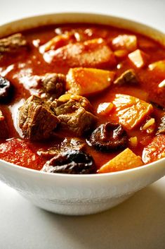 a white bowl filled with meat and vegetable soup on top of a table next to a spoon