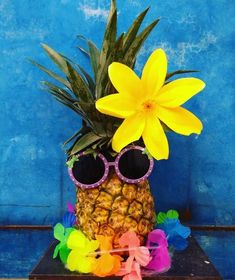 a pineapple with sunglasses and flowers in front of a blue wall