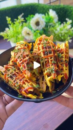 someone holding up a plate of food with noodles and sauces on it in front of a potted plant