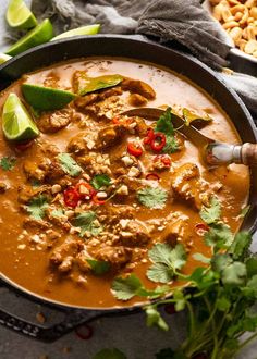 a bowl filled with meat and vegetables next to cilantro, lime wedges and peanuts