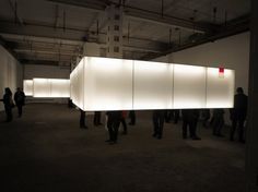 people are standing around in an empty room with white walls and lights on the ceiling