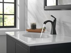 a black faucet sitting on top of a bathroom sink next to a window