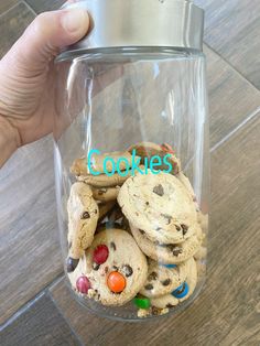 a hand holding a glass jar filled with cookies and m & m's in it