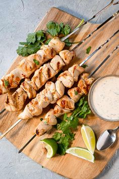 chicken skewers on a cutting board with dipping sauce and cilantro garnishes