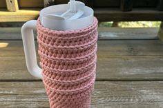 a pink knitted coffee cup holder on a picnic table with an insulated lid