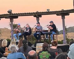 three men are playing music on stage in front of an audience at the outdoor event