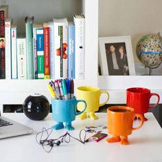 a laptop computer sitting on top of a desk next to two mugs and books