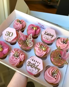 a box filled with lots of pink cupcakes covered in frosting and gold decorations