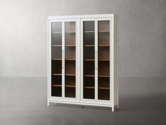 a tall white bookcase with glass doors on the front and bottom, in an empty room