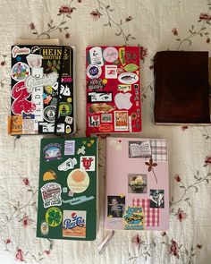 four notebooks with stickers on them are laying on a floral bed spread, one is brown and the other has pink flowers