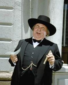 a man in a black suit and hat holding a knife