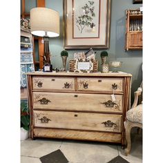 an old dresser is sitting in front of a lamp and pictures on the wall behind it