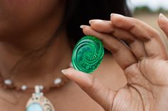 a close up of a person holding a green object in their hand and wearing a necklace