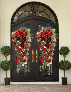 two christmas wreaths on the front door of a house with potted plants and trees