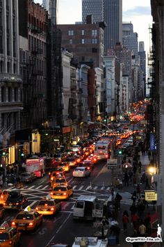 a city street filled with lots of traffic next to tall buildings in the evening time