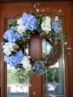 a wreath with blue and white flowers is hanging on a front door, next to a window