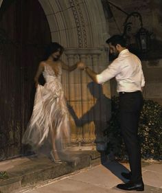 a man standing next to a woman in front of a door holding hands with her