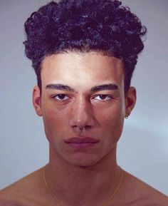 a young man with curly hair and piercings on his nose looking at the camera