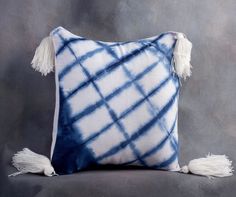 a blue and white pillow with tassels on the sides, sitting against a gray background