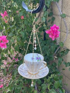 a teacup hanging from a chain in front of some pink flowers and greenery