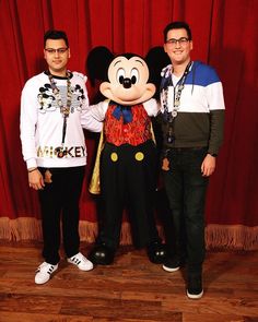 two men standing next to each other in front of a mickey mouse mascot at an event