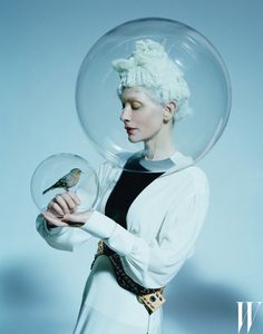 a woman holding a bird in her hand under a glass dome with a bird on it