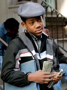 a young boy holding money in his hands and wearing a hat on top of his head