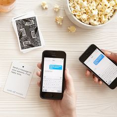 two people are using their cell phones at a table with popcorn and movies on it