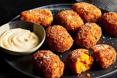 some fried food on a black plate with a small bowl of mayonnaise next to it