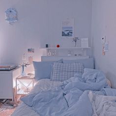 an unmade bed in a white room with blue comforter and pillows on it