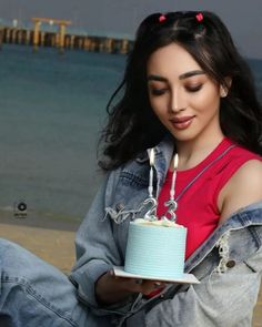 a woman sitting on the beach holding a cake with candles in her hand and looking at it