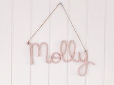 the word melly is hanging from a string on a white wall with wood planks