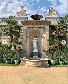 a fountain surrounded by potted plants in front of a building with statues on it