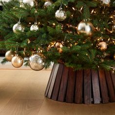 a christmas tree with gold and silver ornaments in a wooden basket on the floor next to a fireplace