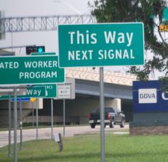 two green street signs sitting next to each other on the side of a road in front of a highway