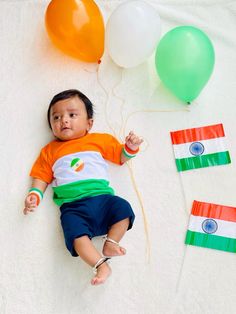 a baby laying on the ground next to balloons and streamers with india flag colors