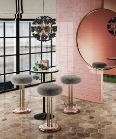 three stools with fur on them in front of a pink wall and round mirror