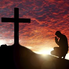 a man kneeling in front of a cross at sunset