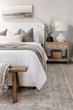 a bed with white sheets and pillows in a bedroom next to a wooden table on the floor