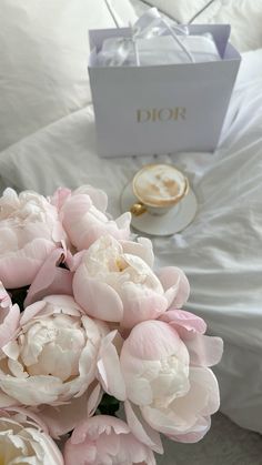 a bouquet of pink flowers sitting on top of a bed next to a cup and saucer