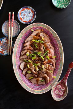 a plate with meat and vegetables on it next to chopsticks, bowls and spoons