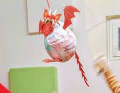 a paper mache dragon flying through the air next to a green chair and wall