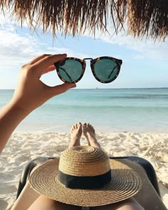 a person laying on top of a sandy beach next to the ocean wearing sunglasses and a straw hat