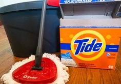 a red mop sitting on top of a wooden floor next to a box of tide