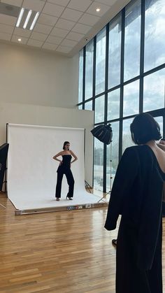 a woman is standing in front of a white backdrop while another person takes a photo