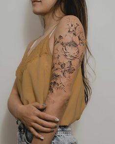 a woman with a flower tattoo on her arm is posing in front of a white wall