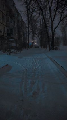 a snowy street at night with buildings in the background